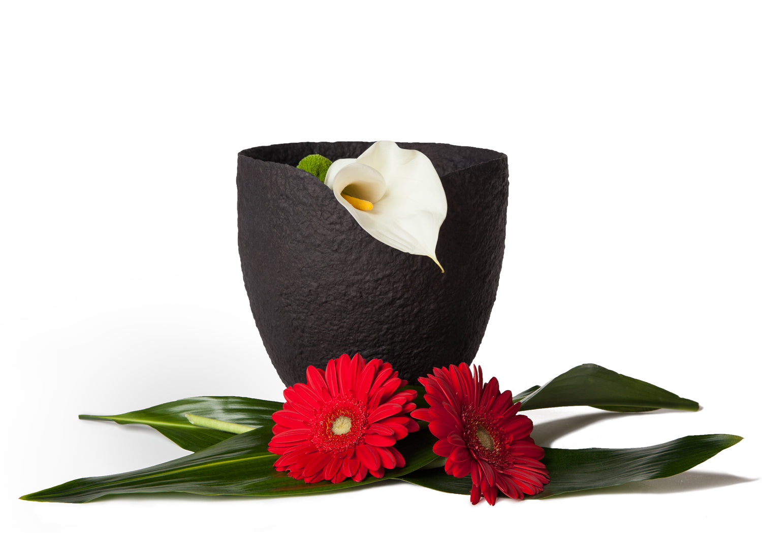 Picture of a black ovoid biodegradable cremation urn on sale at Muses Design Urns. View with flowers.